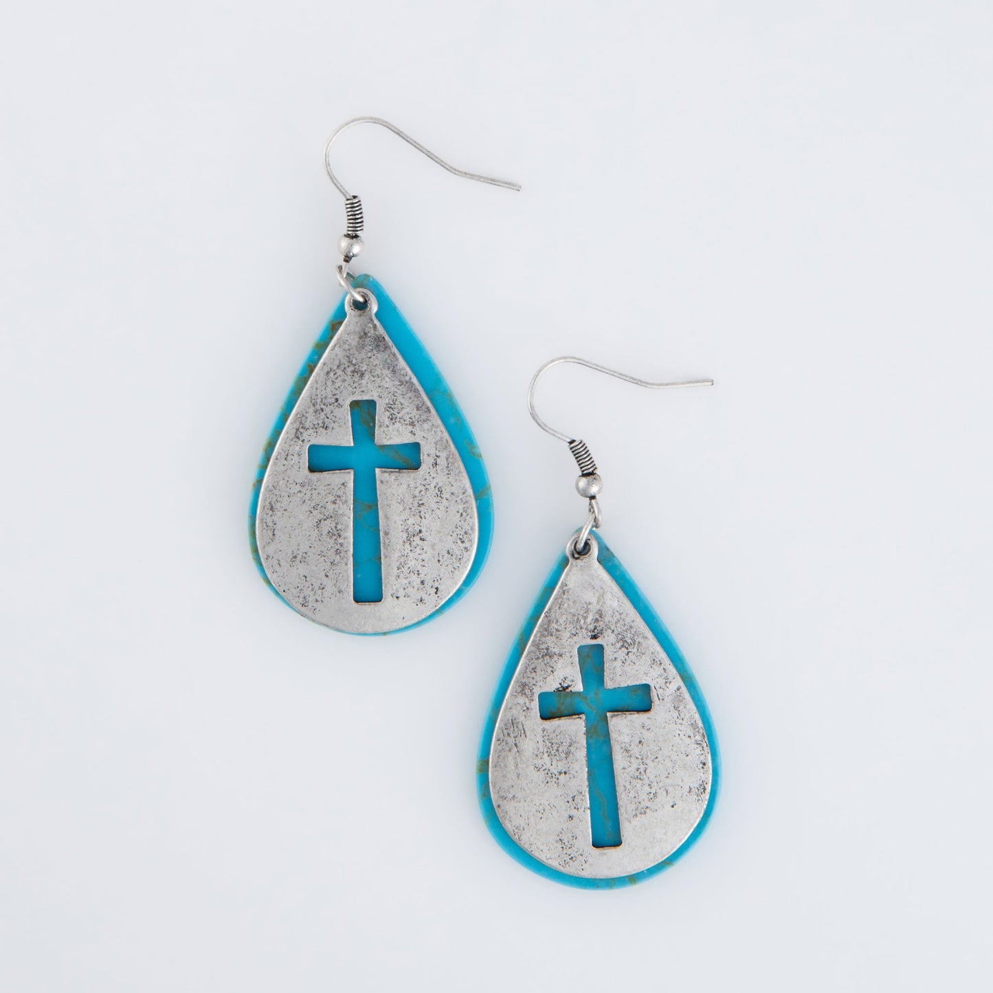 A pair of turquoise teardrop-shaped earrings with silver crosses dangled from their centers