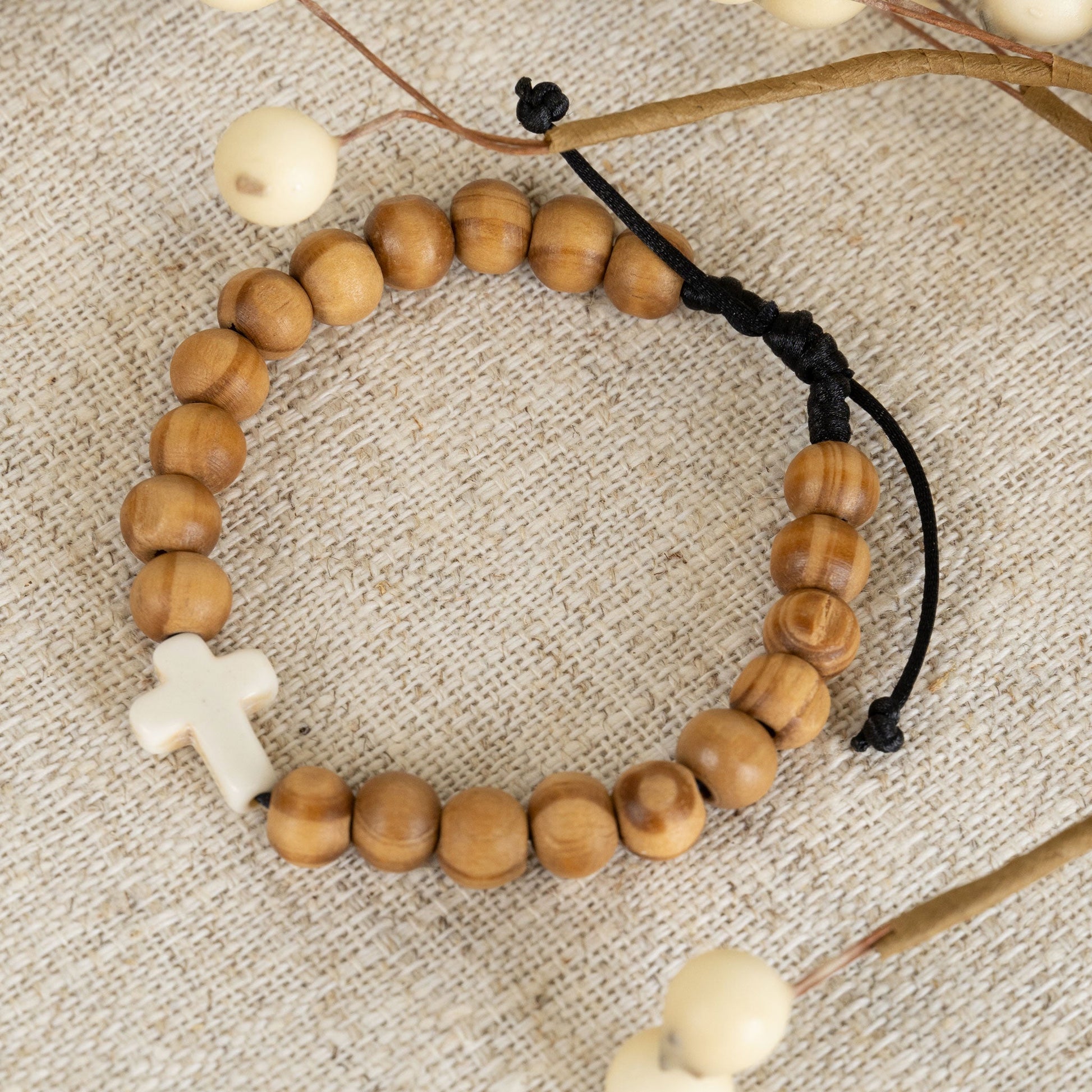 A beaded bracelet with round wood beads and a white cross charm, displayed on a textured background with some decorative elements.