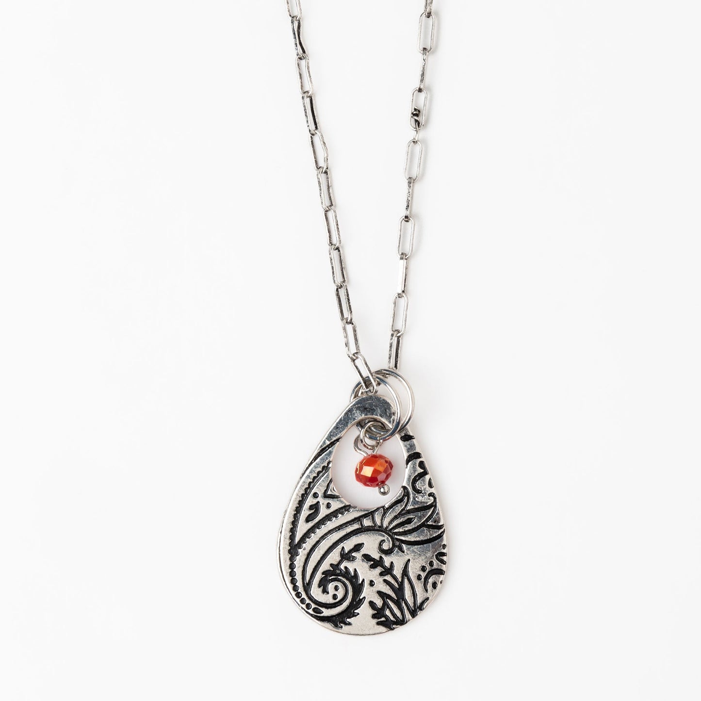 A silver chain pendant necklace with a teardrop-shaped paisley design pendant and a red bead