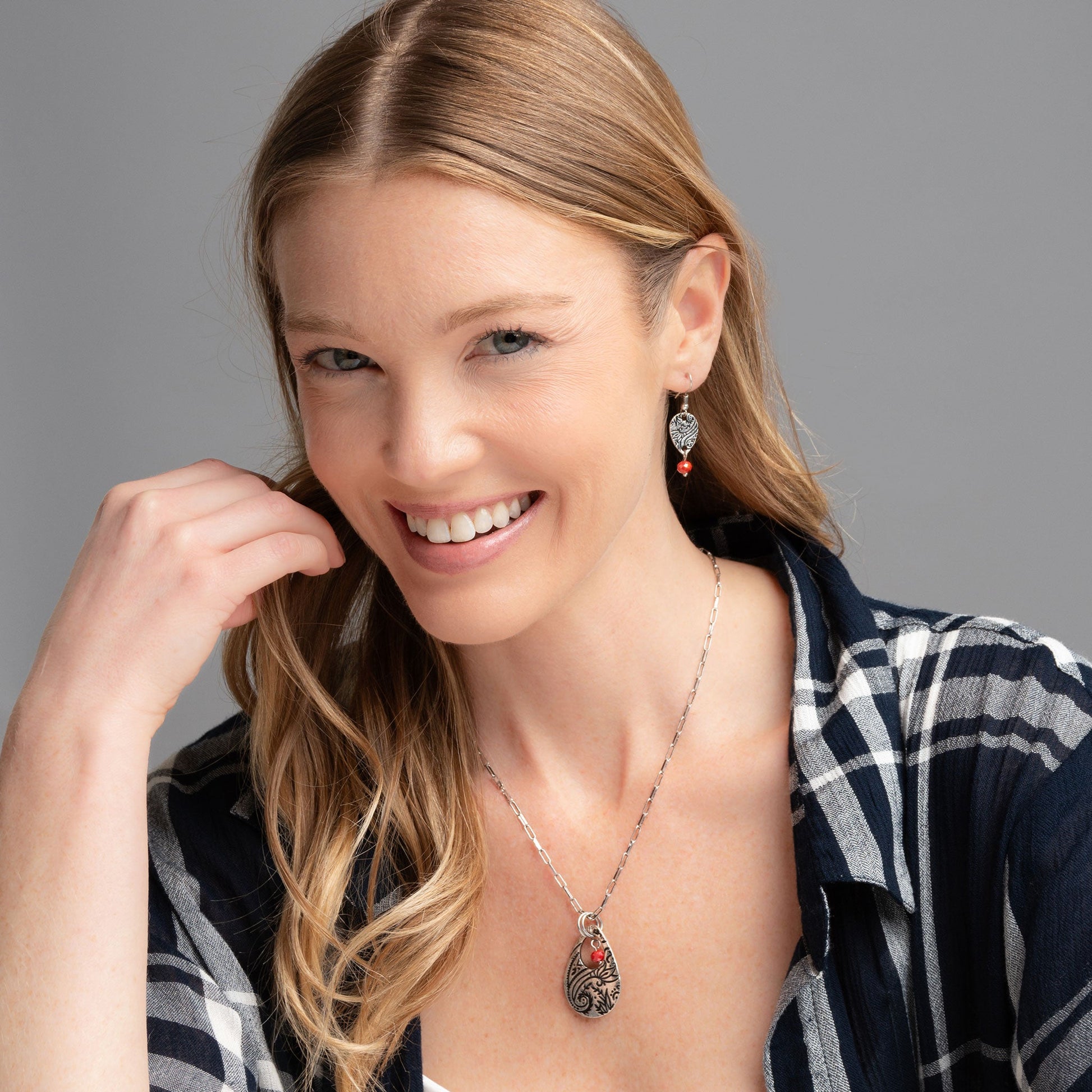 A woman wearing a silver chain pendant necklace with a teardrop-shaped paisley design pendant and a red bead