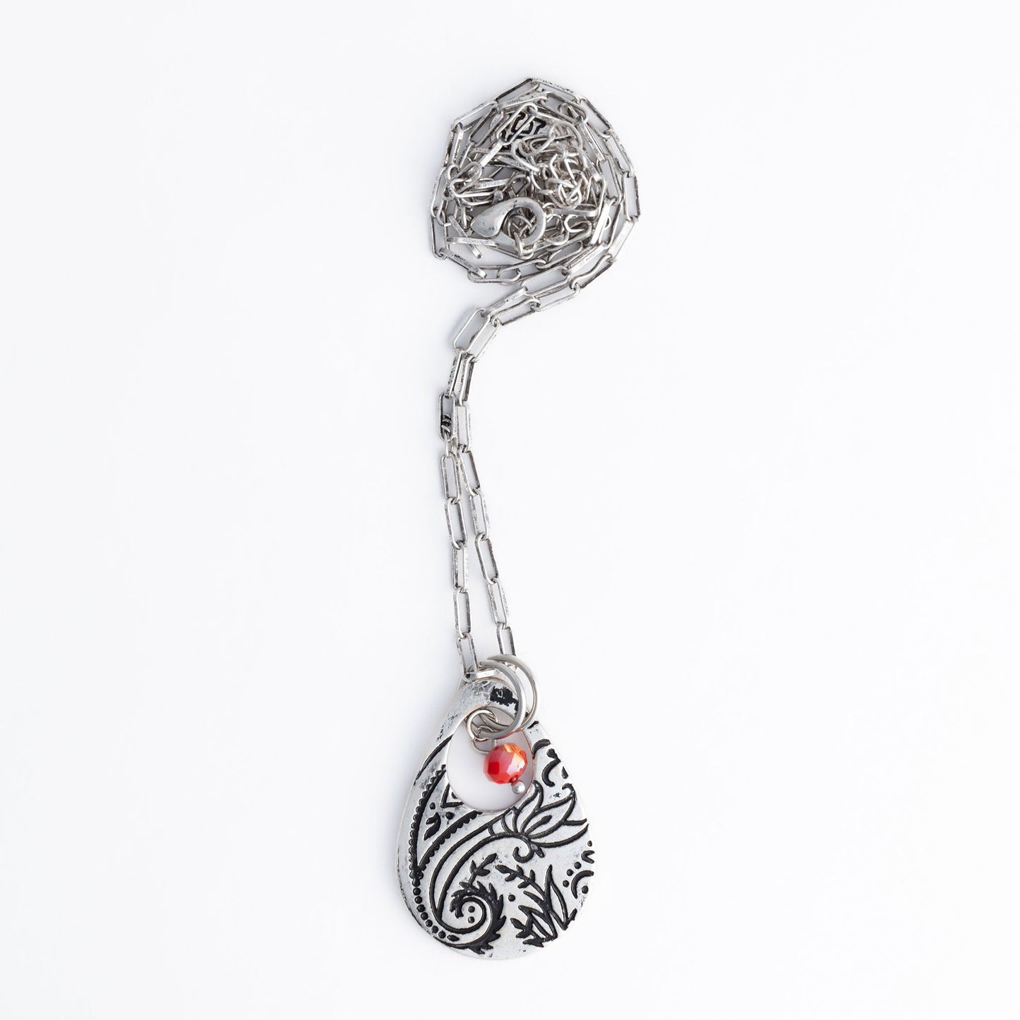 A silver chain pendant necklace with a teardrop-shaped paisley design pendant and a red bead