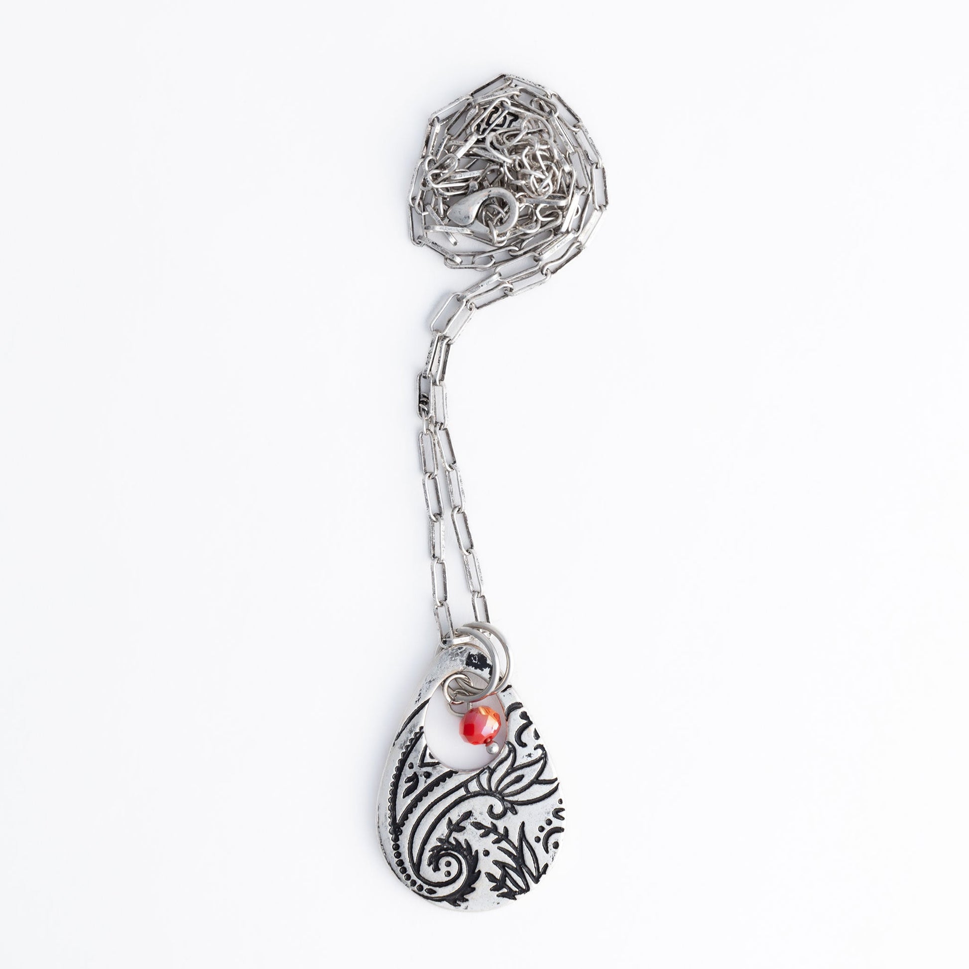 A silver chain pendant necklace with a teardrop-shaped paisley design pendant and a red bead