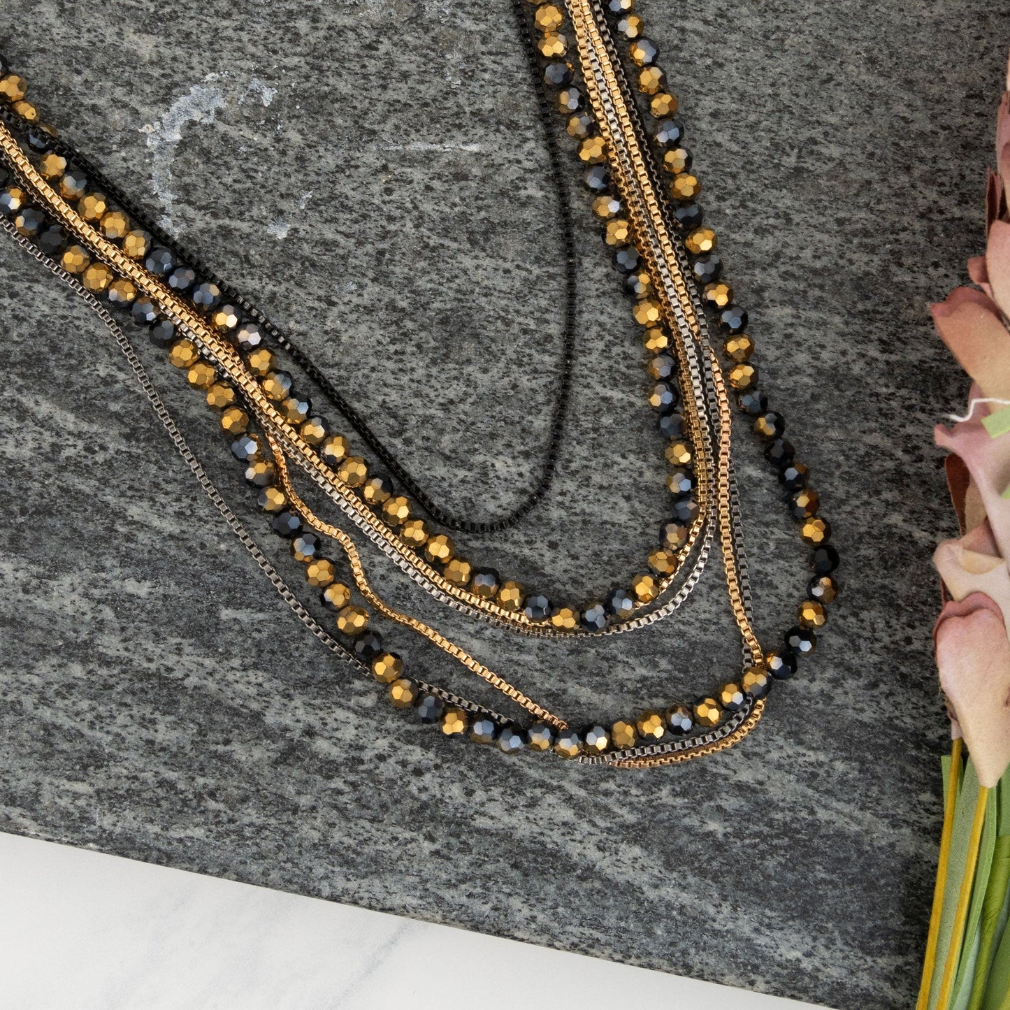 A two-toned, layered necklace with black and gold beads displayed on a gray surface.