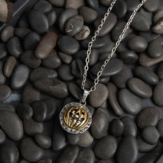 A two-toned pumpkin pendant necklace with a silver chain displayed against a background of dark stones.
