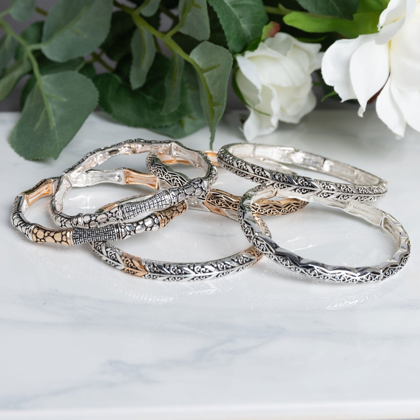 A group of silver and gold stretch bracelets sitting on a marble table