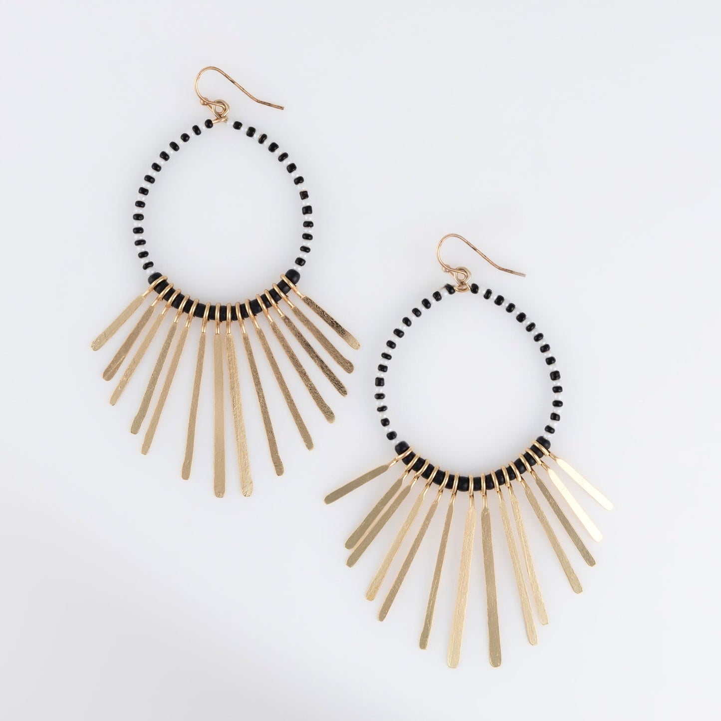 A pair of Andra Fringe Earrings with black beaded hoops and gold fringe.