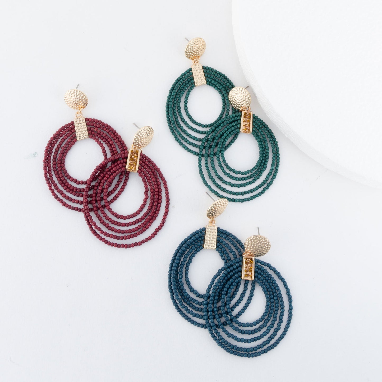 A collection of three hoop seed bead earrings in red, green, and blue, each with gold detailing and attached to gold-colored posts.