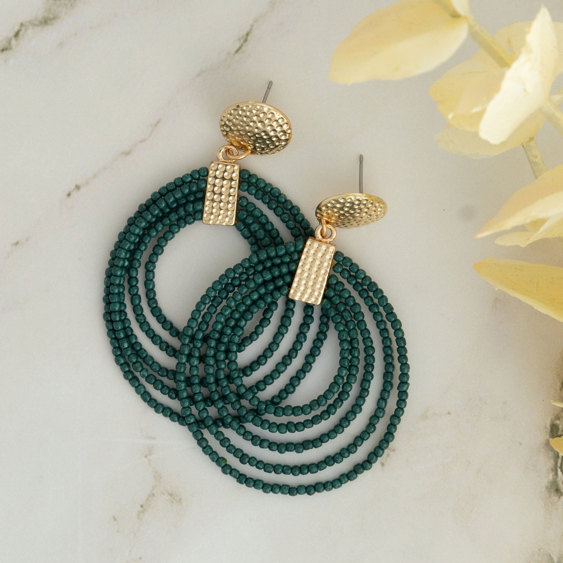 A pair of hoop earrings made of green seed beads with gold detailing at the top, displayed on a marble surface.