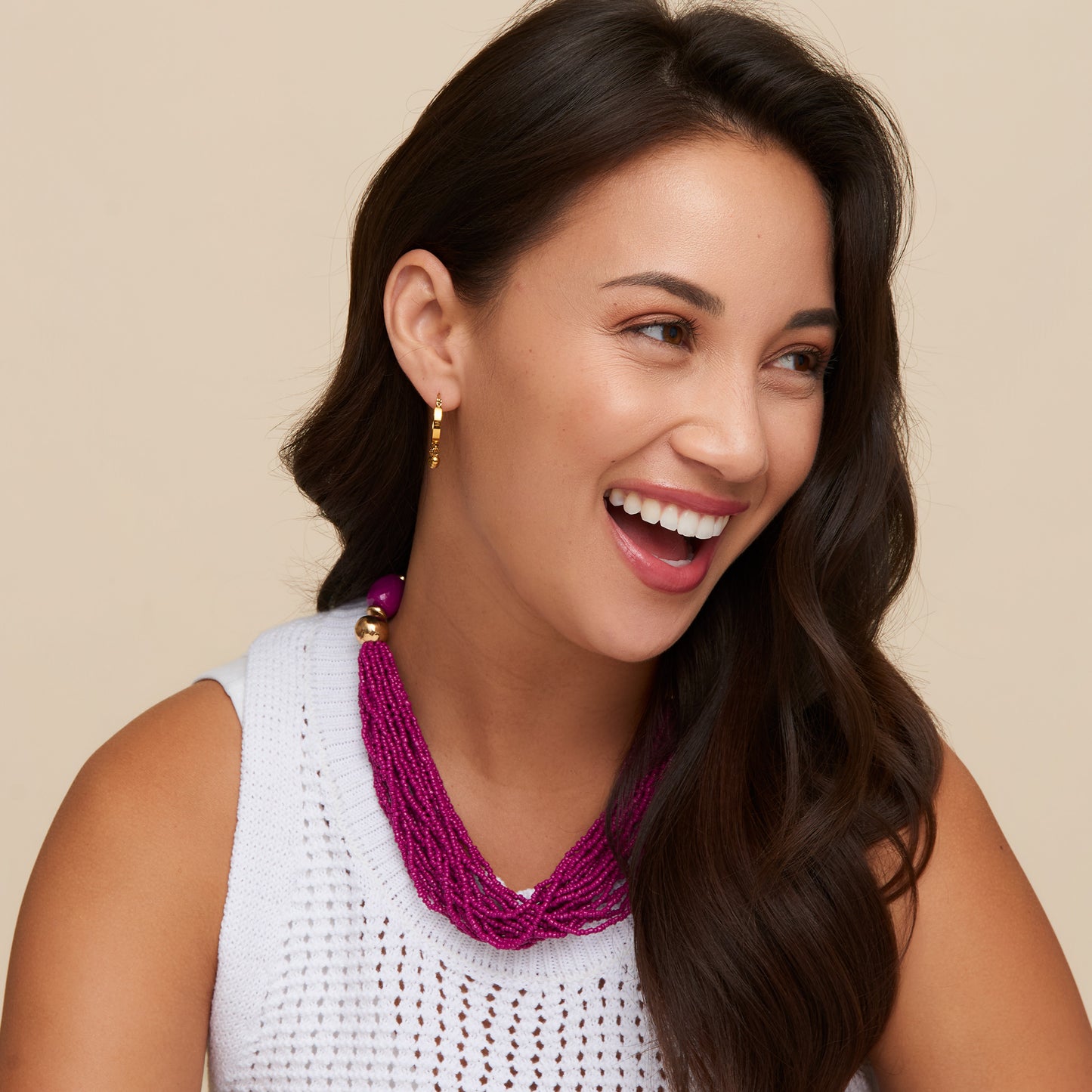 Woman wearing a white sleeveless top and a purple beaded necklace against a beige background