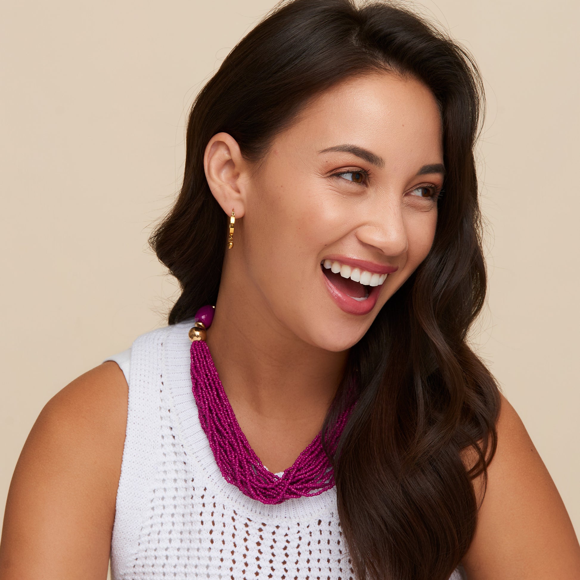 Woman wearing a white sleeveless top and a purple beaded necklace against a beige background