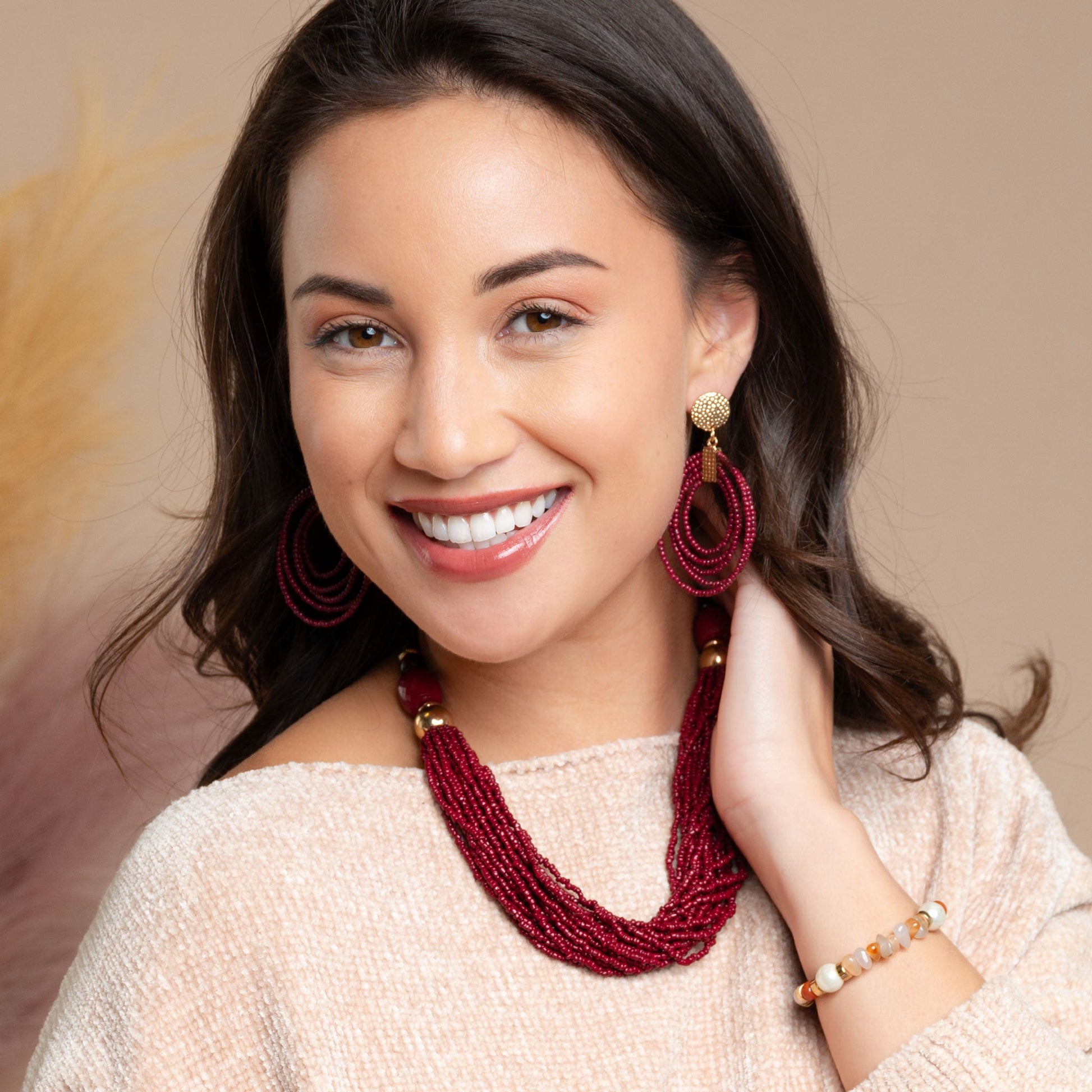 A woman wearing a multi-strand red seed bead necklace with coordinating seed bead earrings
