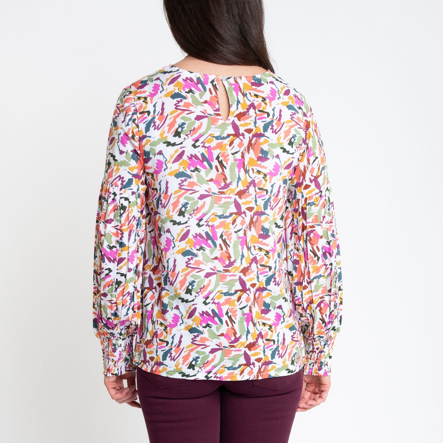 A woman wearing a multicolored balloon sleeve blouse with a round neckline, paired with purple trousers.