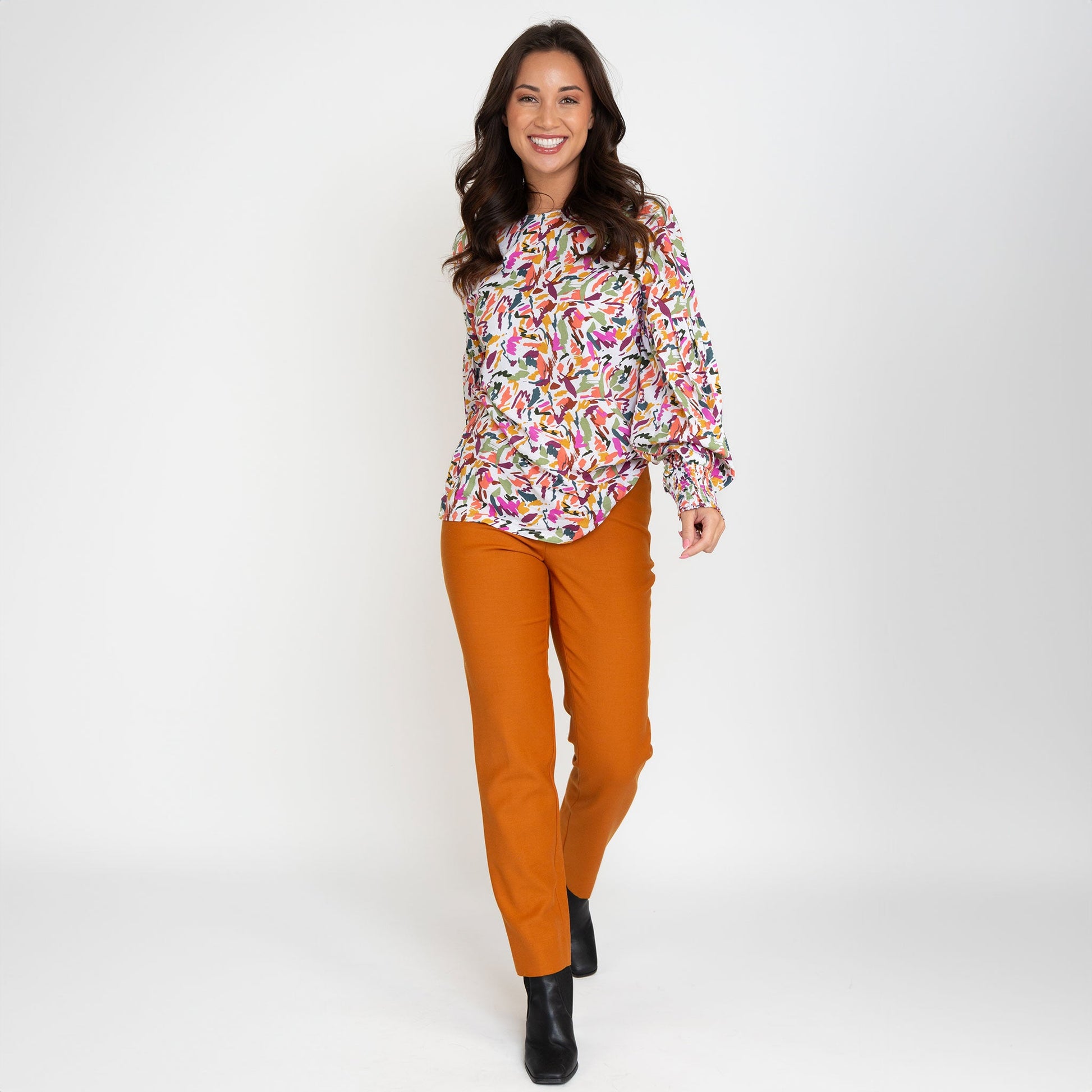 A woman wearing a multicolored balloon sleeve blouse with a round neckline, paired with orange trousers.