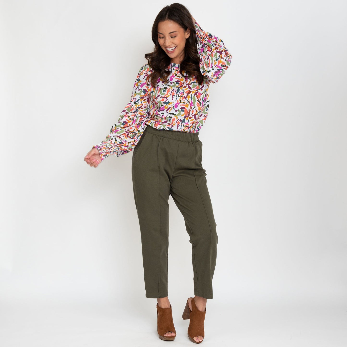 A woman wearing a multicolored balloon sleeve blouse with a round neckline, paired with green trousers.