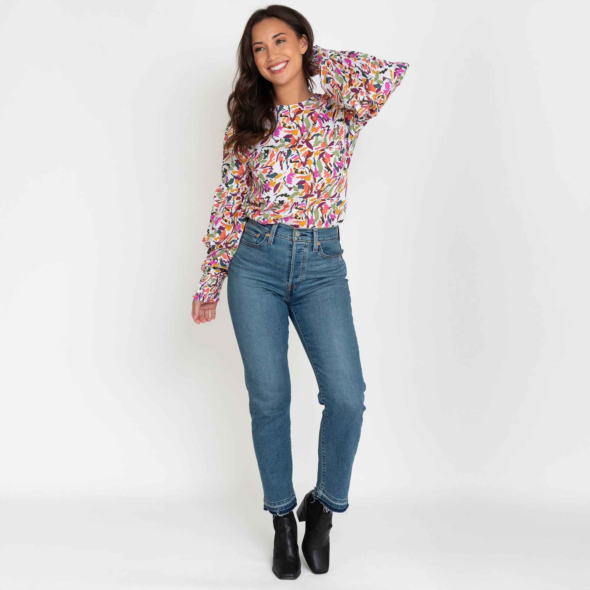 A woman wearing a multicolored balloon sleeve blouse with a round neckline, paired with blue jeans