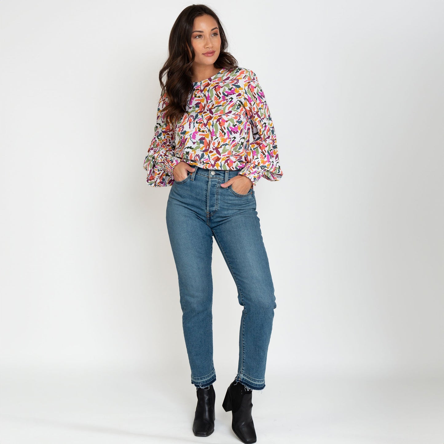 A woman wearing a multicolored balloon sleeve blouse with a round neckline, paired with blue jeans