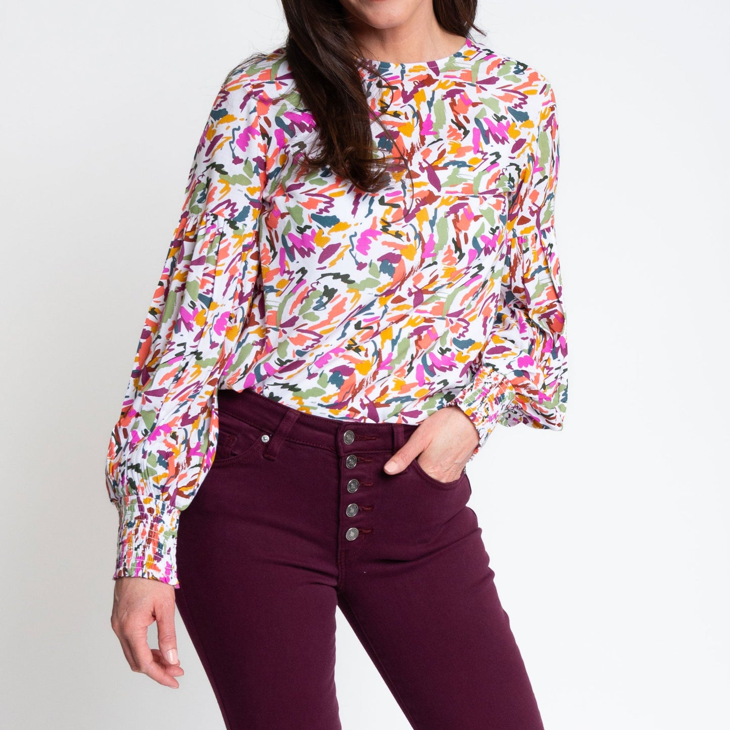 A woman wearing a multicolored balloon sleeve blouse with a round neckline, paired with purple trousers.