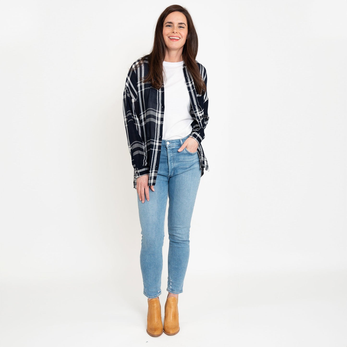 A woman wearing a navy plaid button-up shirt with button-up design and a relaxed fit, paired with light blue jeans and boots.
