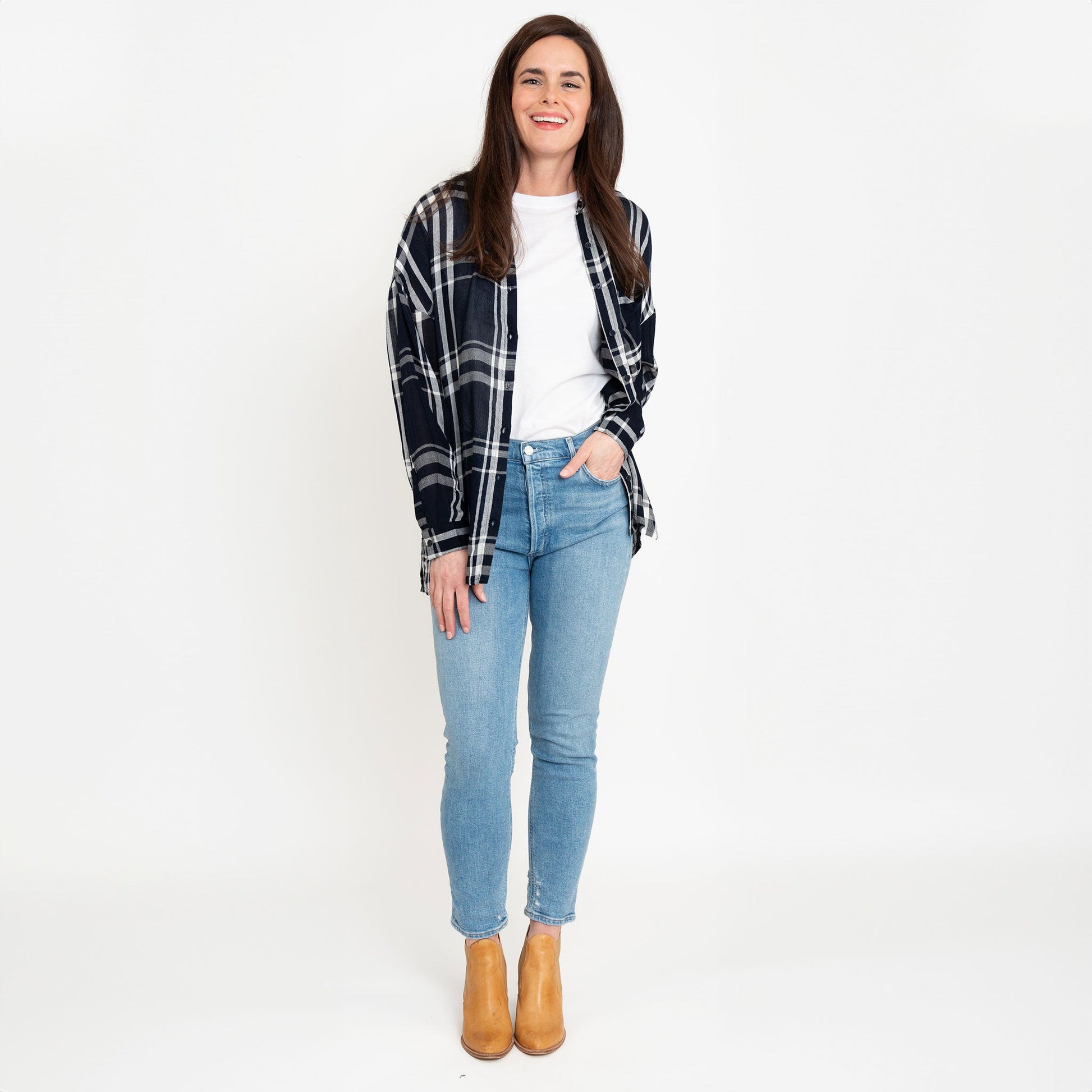 A woman wearing a navy plaid button-up shirt with button-up design and a relaxed fit, paired with light blue jeans and boots.