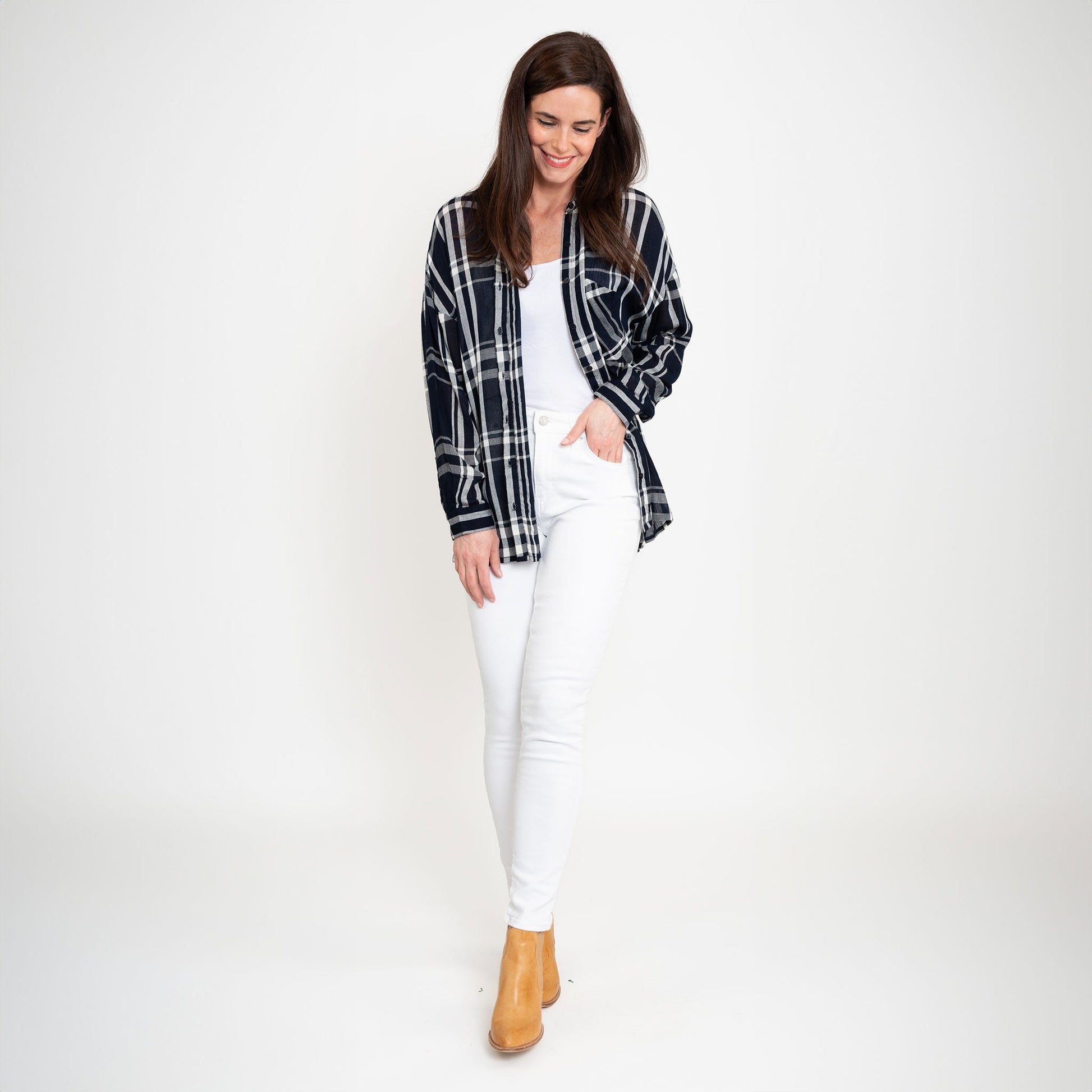 A woman wearing a navy plaid button-up shirt with button-up design and a relaxed fit, paired with white jeans and boots.