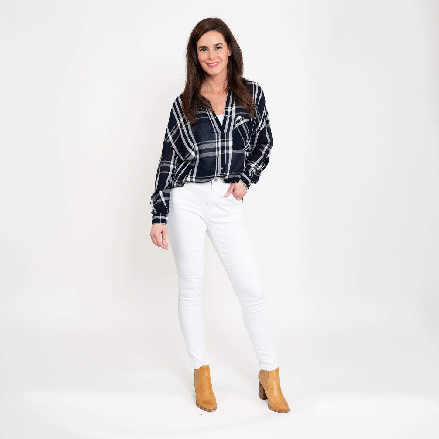 A woman wearing a navy plaid button-up shirt with button-up design and a relaxed fit, paired with white jeans and boots.