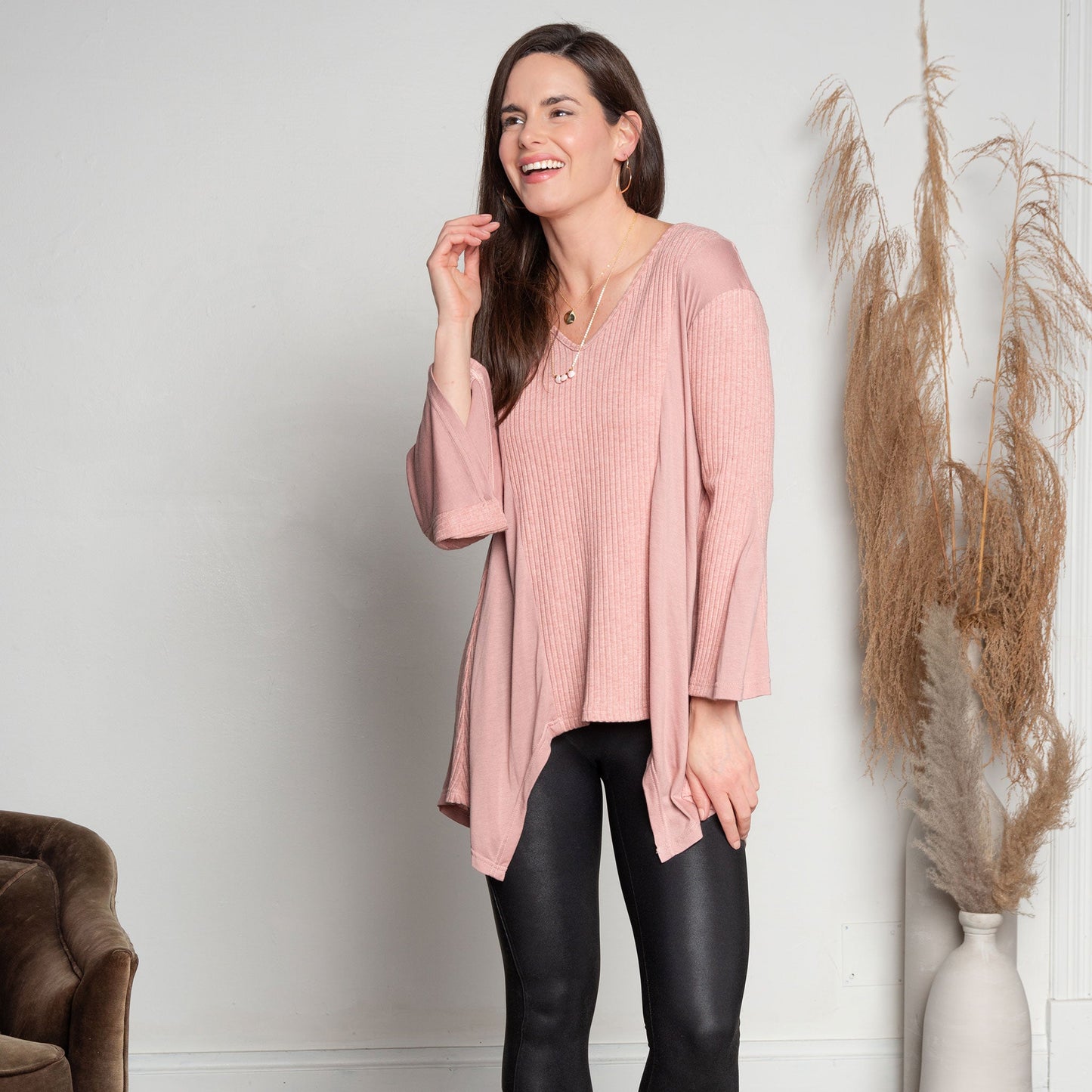 A woman wearing a strawberry pink tunic top with bell sleeves and a v-neck, paired with black leather leggings