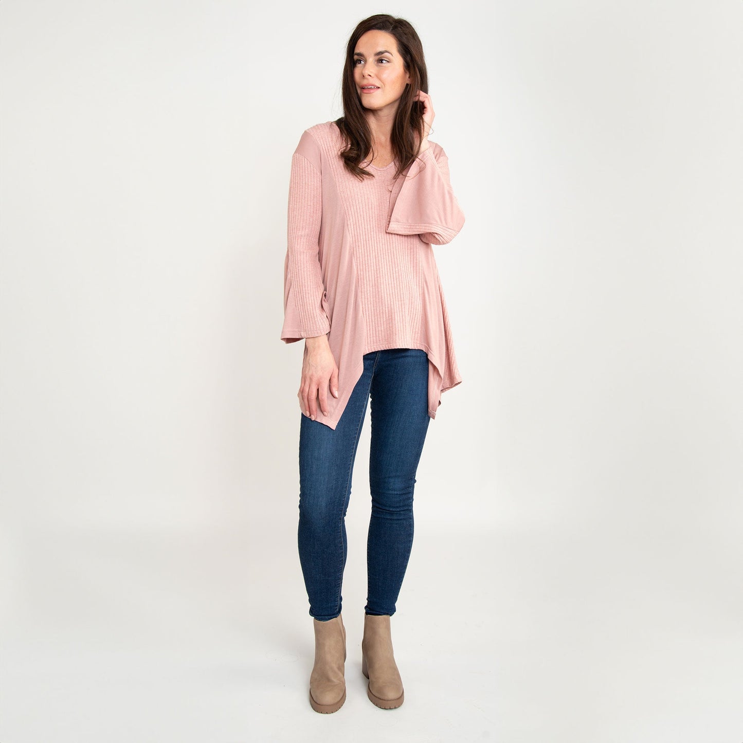 A woman wearing a strawberry pink tunic top with bell sleeves and a v-neck, paired with blue jeans.