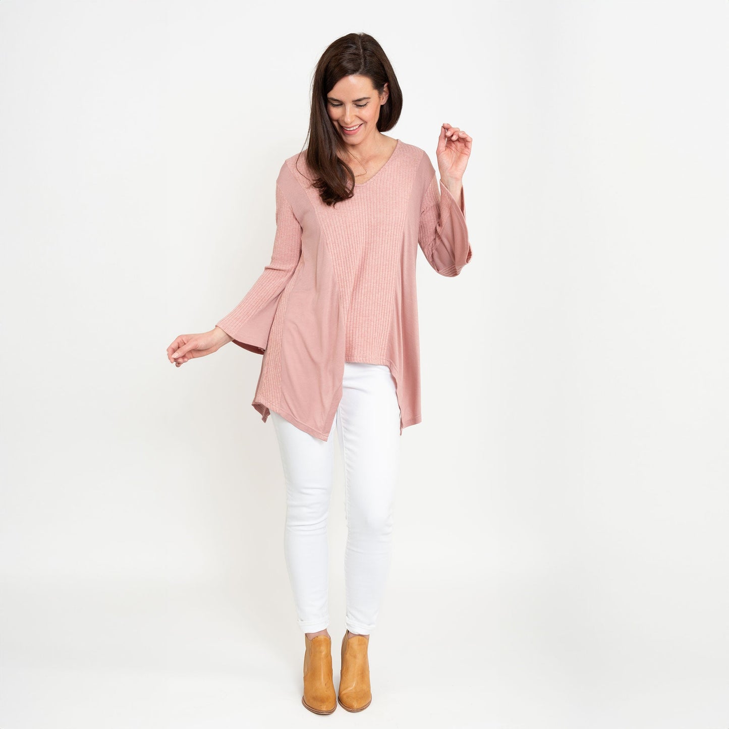 A woman wearing a strawberry pink tunic top with bell sleeves and a v-neck, paired with white pants.