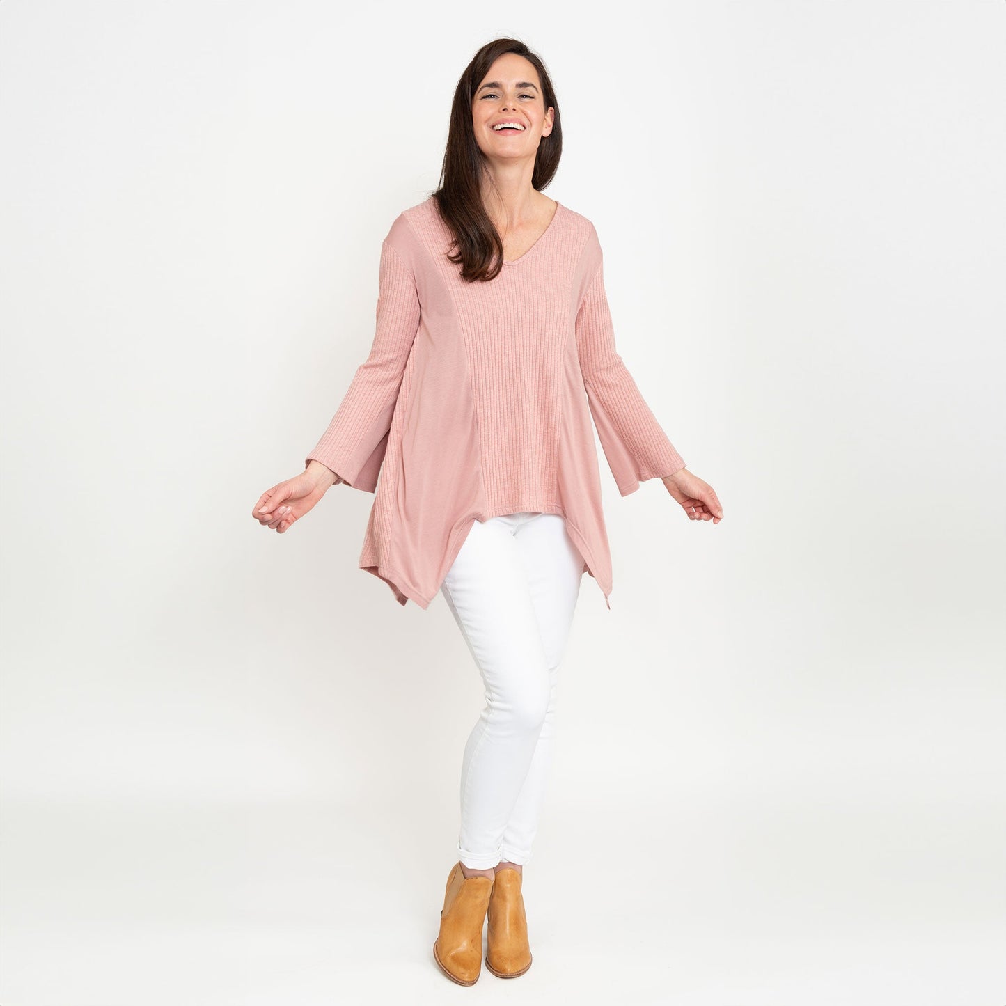A woman wearing a strawberry pink tunic top with bell sleeves and a v-neck, paired with white pants.