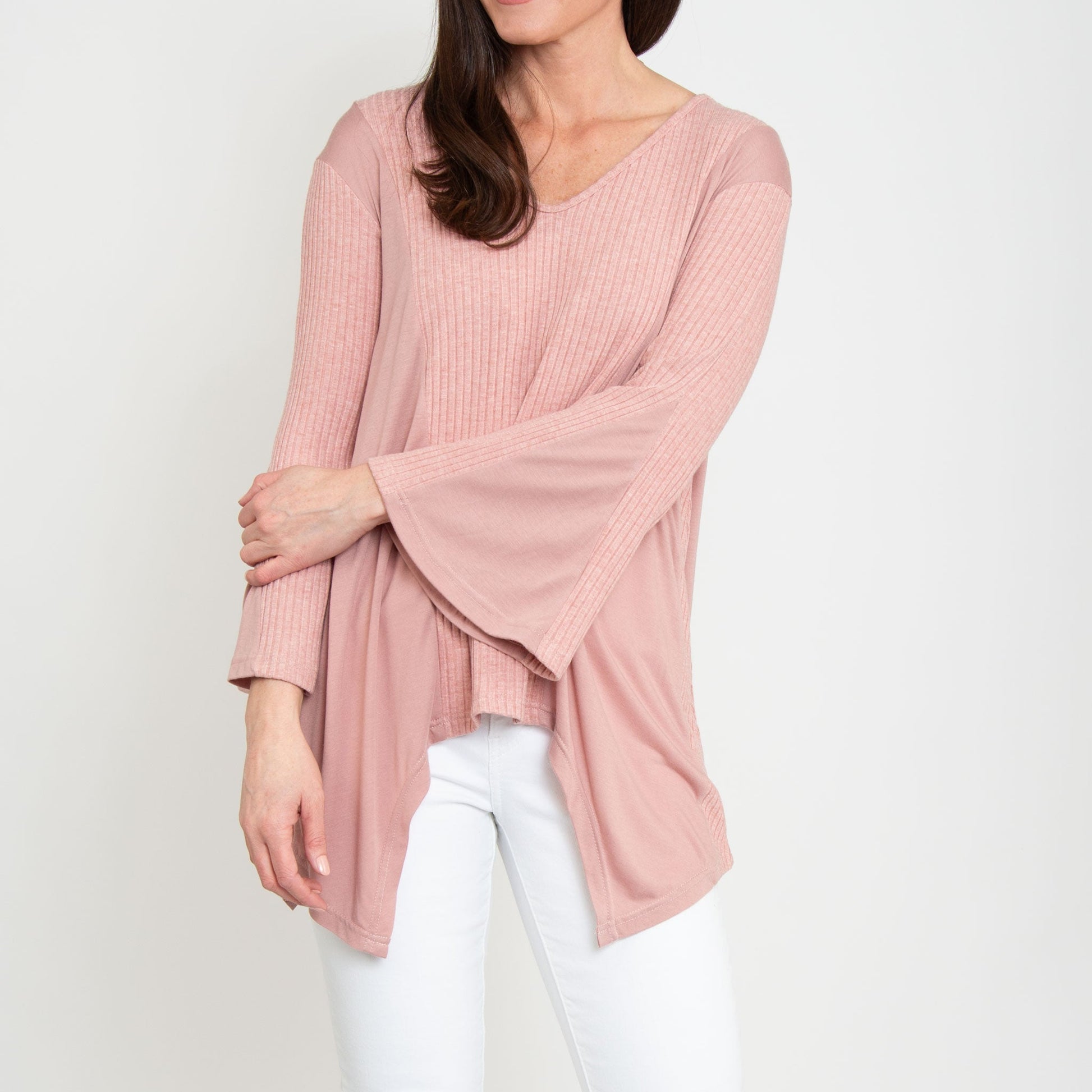 A woman wearing a strawberry pink tunic top with bell sleeves and a v-neck, paired with white pants.
