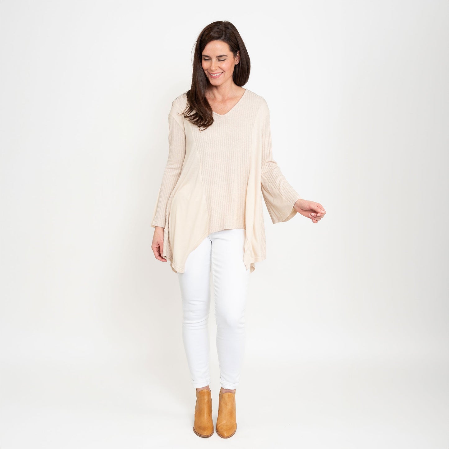 A woman wearing a beige Cassia Bell Sleeve Top with a V-neck and long bell sleeves, paired with white jeans.