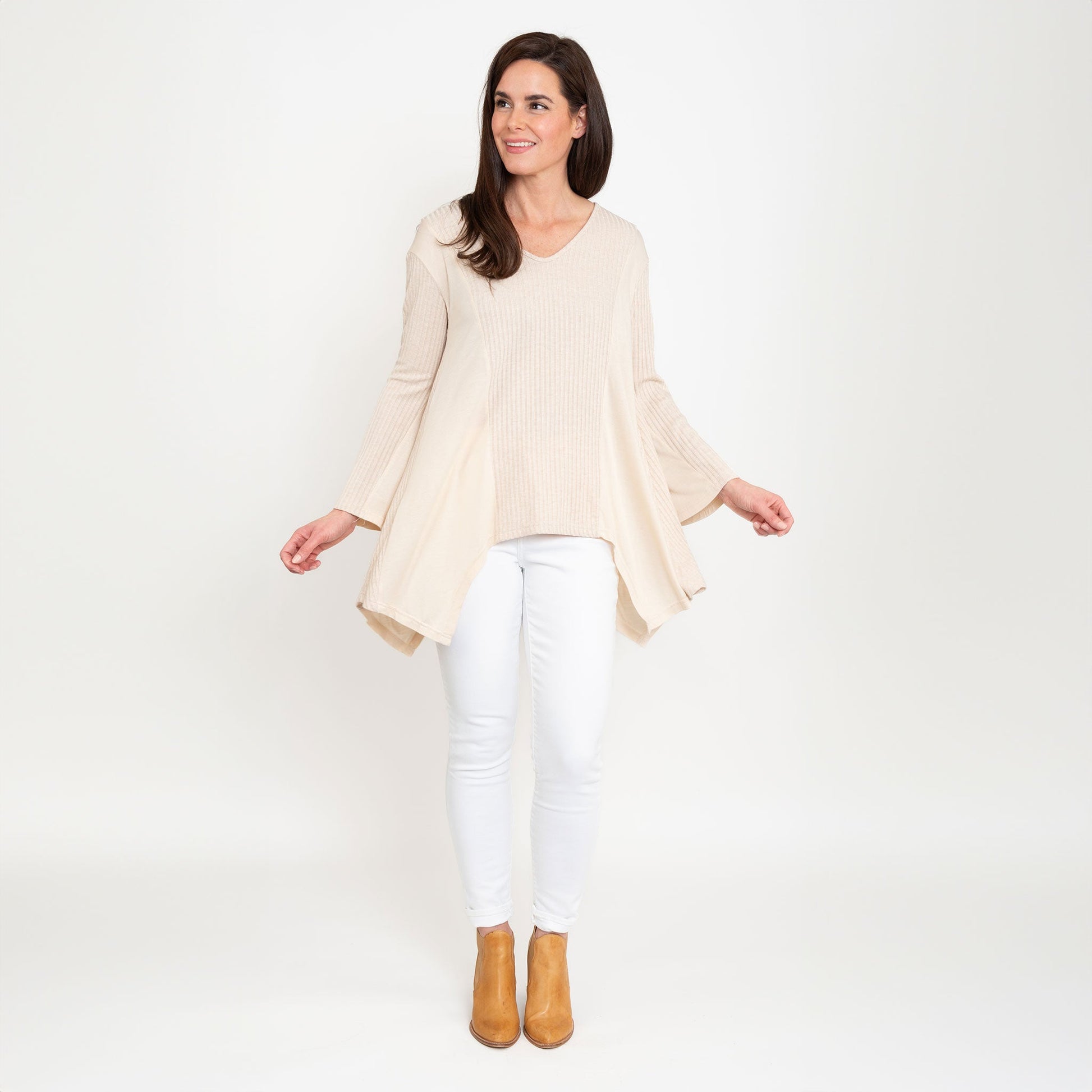 A woman wearing a beige Cassia Bell Sleeve Top with a V-neck and long bell sleeves, paired with white jeans.