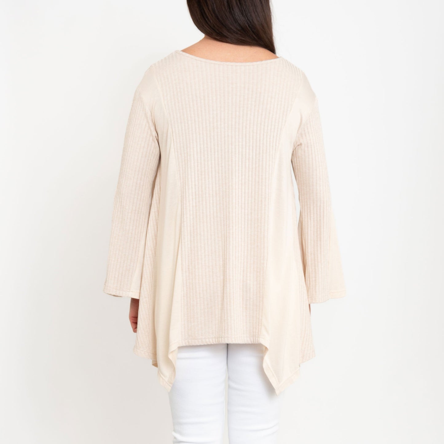 A woman wearing a beige Cassia Bell Sleeve Top with a V-neck and long bell sleeves, paired with white jeans.