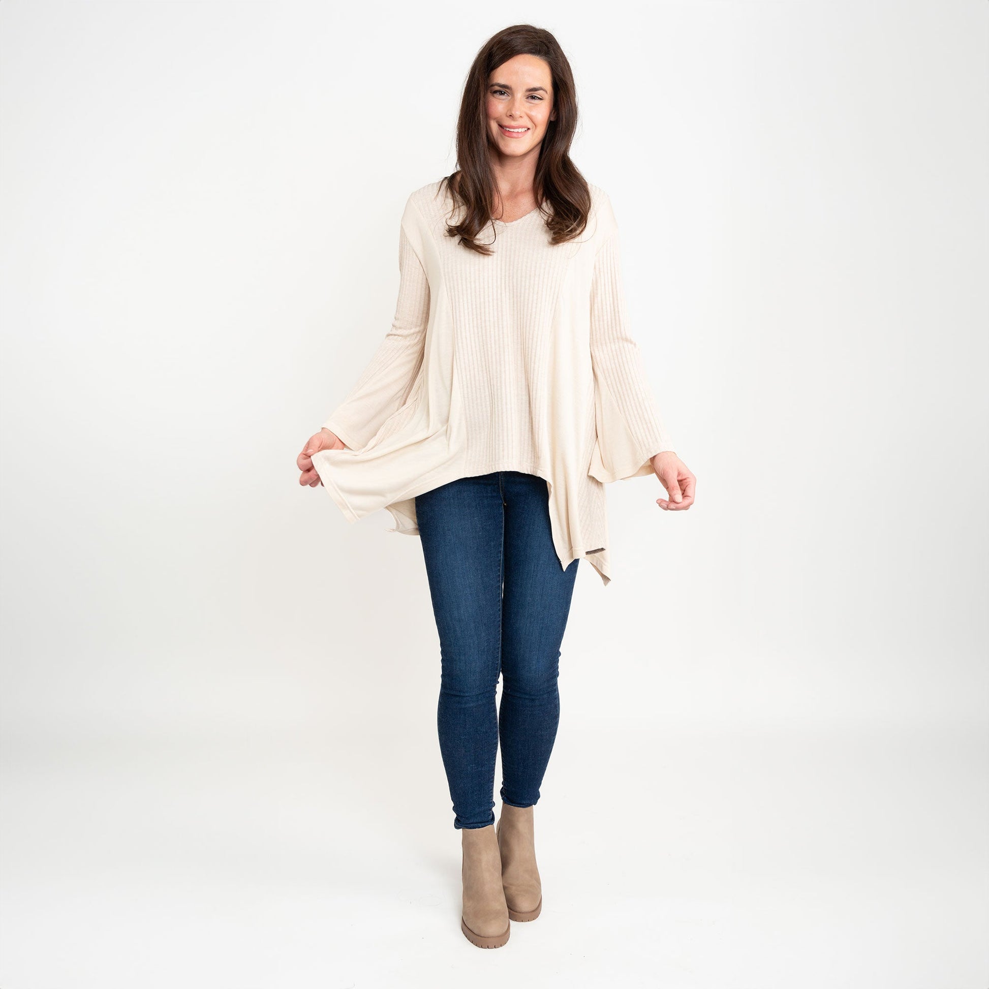 A woman wearing a beige Cassia Bell Sleeve Top with a V-neck and long bell sleeves, paired with blue jeans.