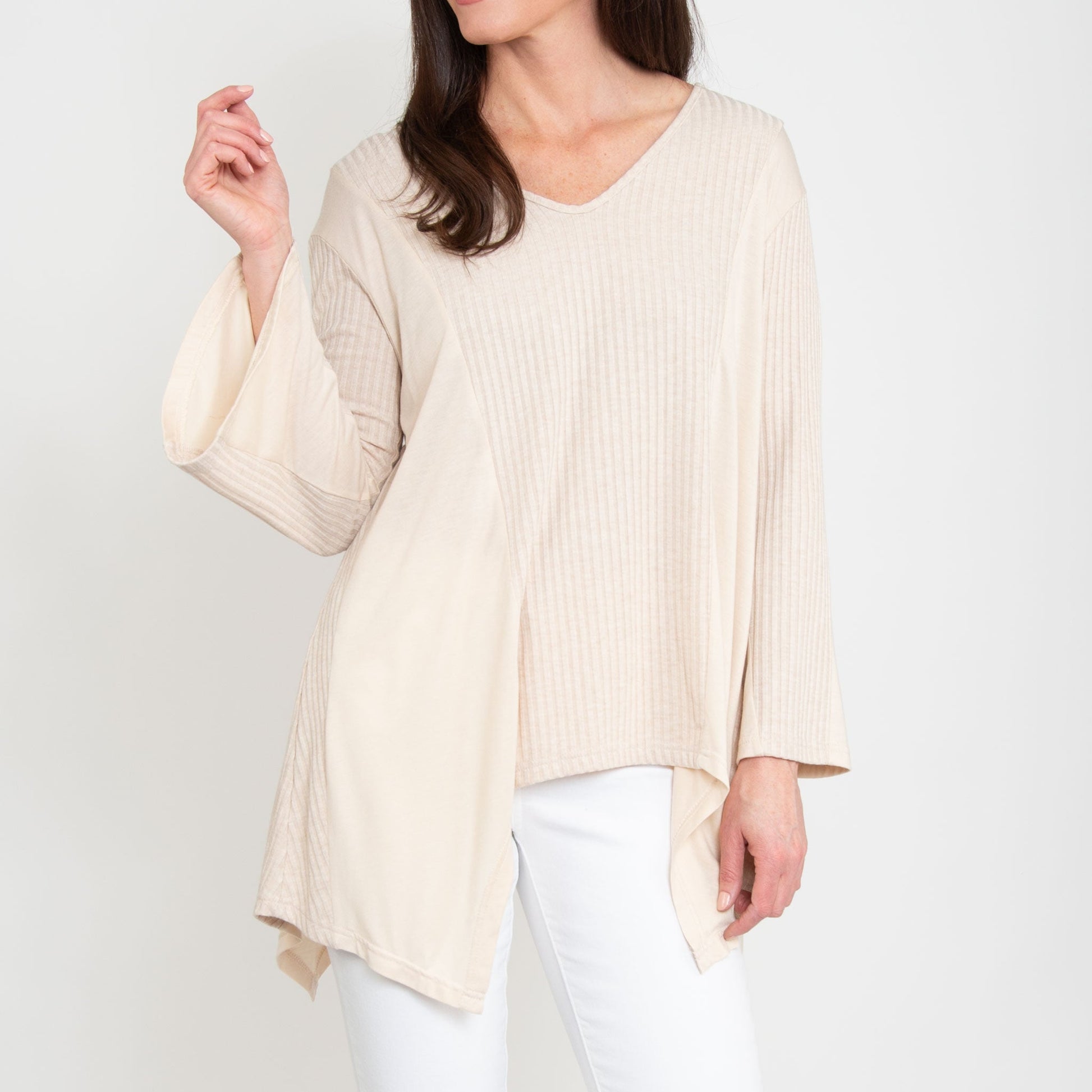 A woman wearing a beige Cassia Bell Sleeve Top with a V-neck and long bell sleeves, paired with white pants.