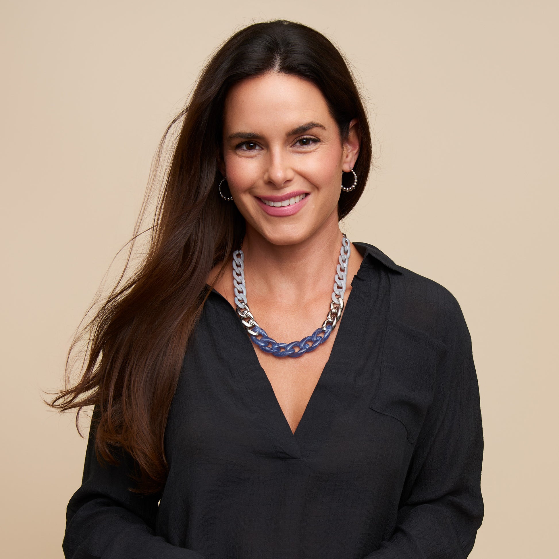 Woman wearing a black shirt and a necklace with a beige background