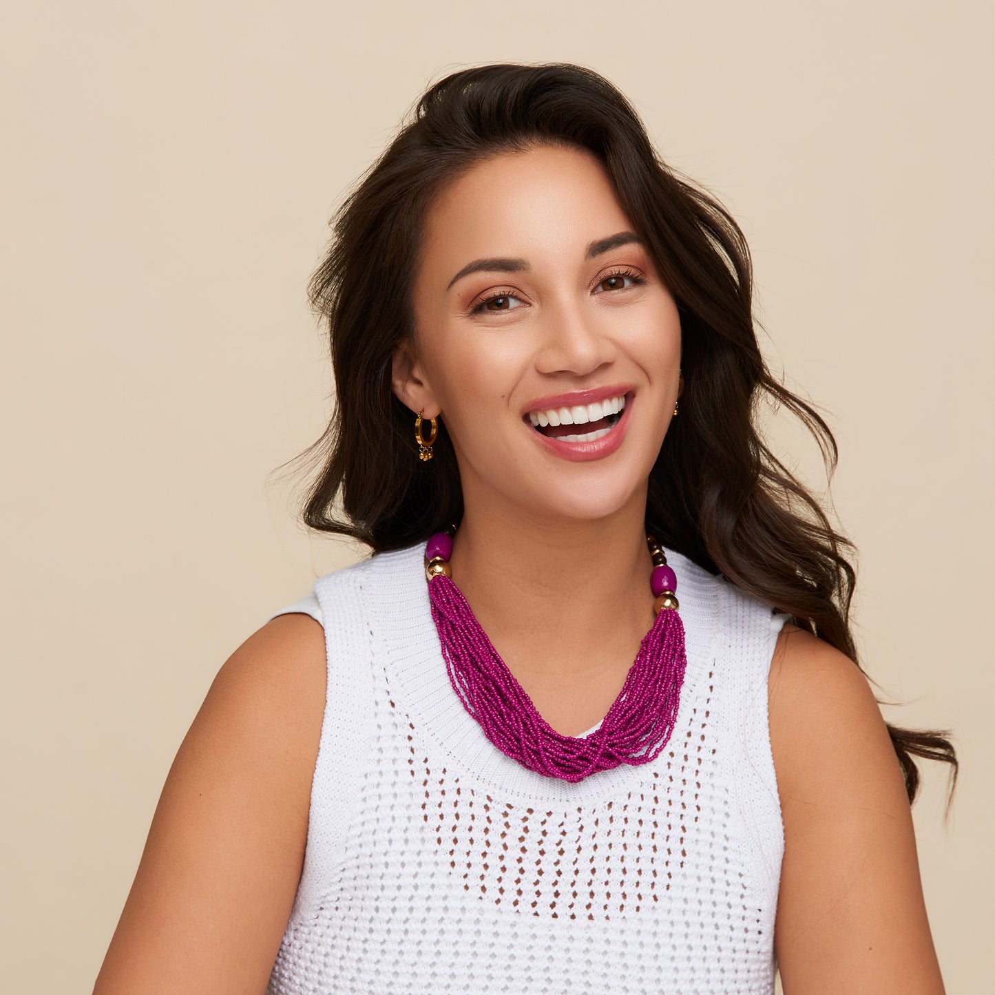 Woman wearing a white sleeveless top and a vibrant pink necklace against a beige background