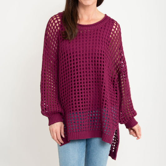 A woman wearing a berry open knit crochet design sweater with long sleeves and a high-low hem.
