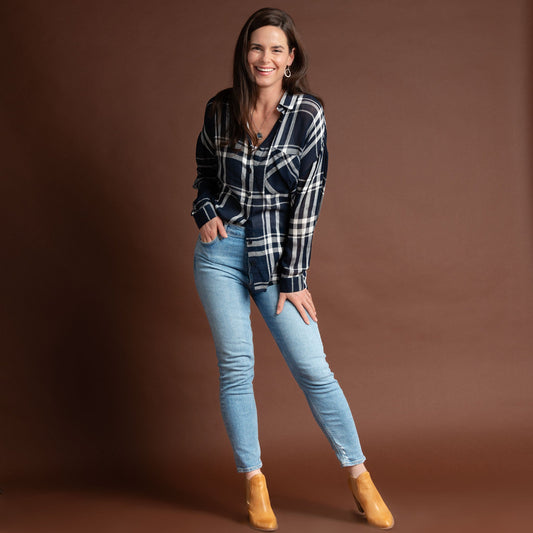 A woman wearing a navy plaid button-up shirt with button-up design and a relaxed fit, paired with light blue jeans and boots.