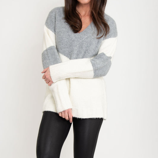 A woman wearing a color block sweater with a V-neck, alternating gray and white blocks, paired with black leggings.