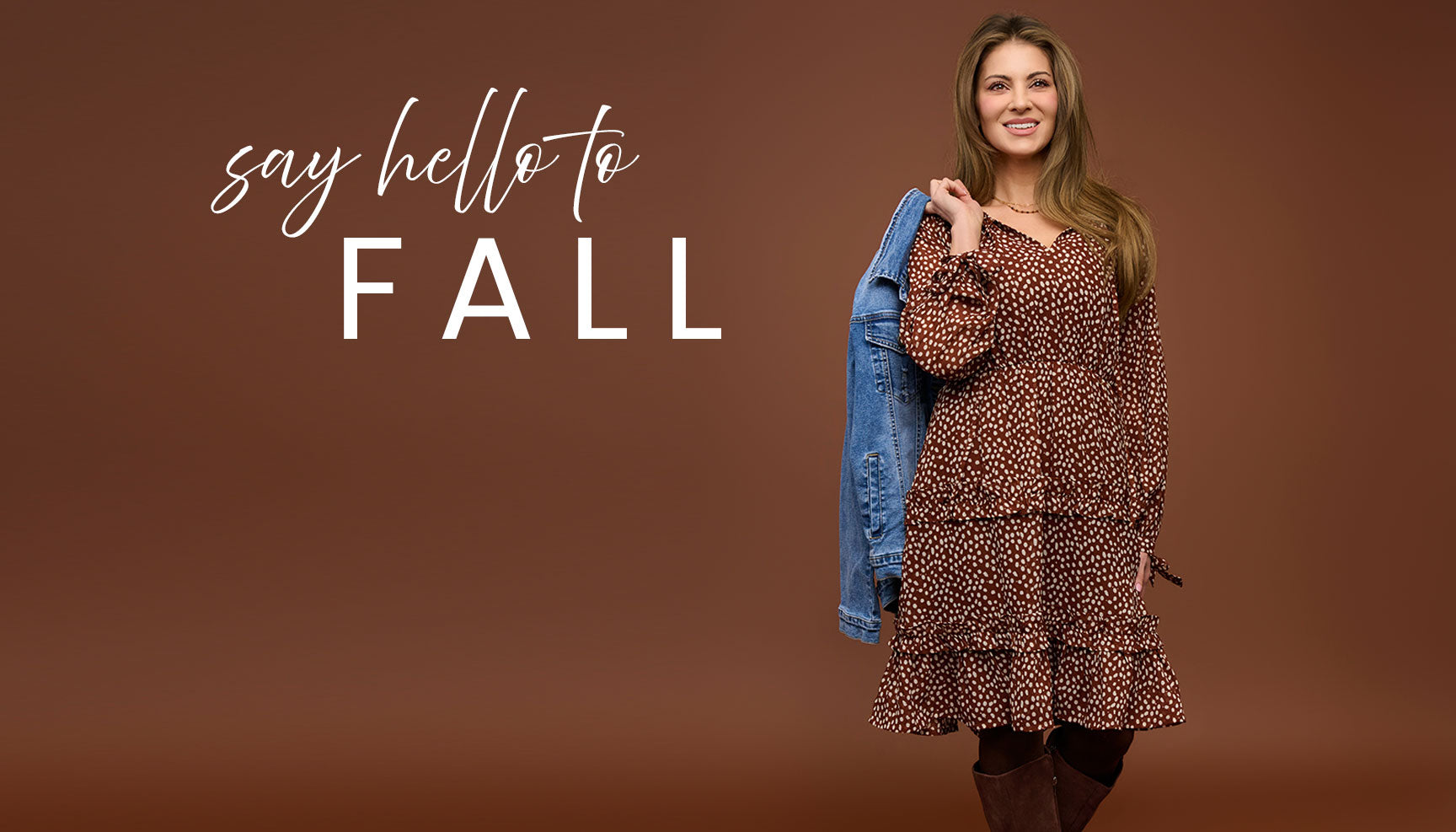 Woman in a polka dot print dress holding a denim jacket with 'say hello to FALL' text on a brown background